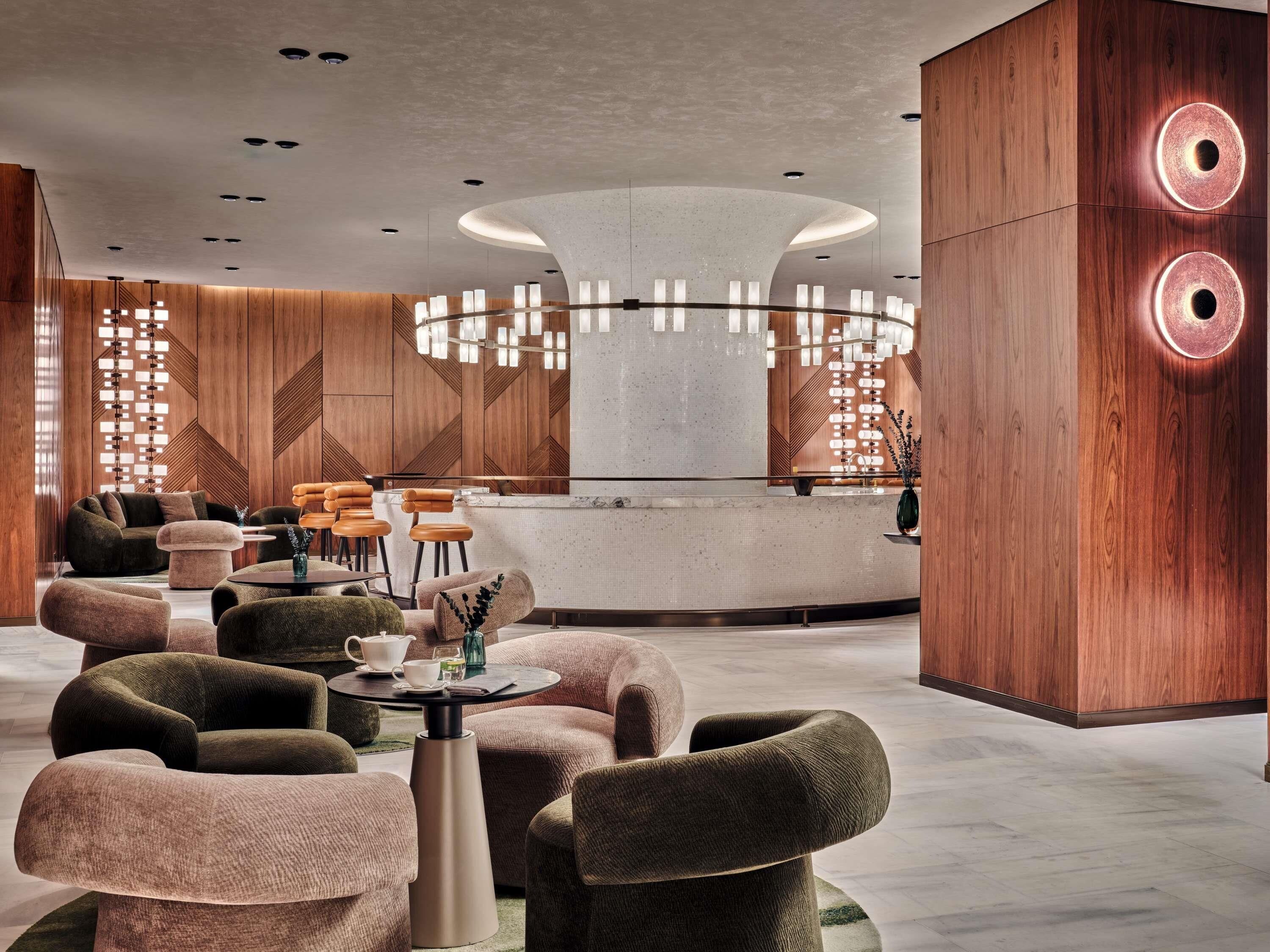 A modern lobby with a central reception desk, seating area, and decorative lighting.