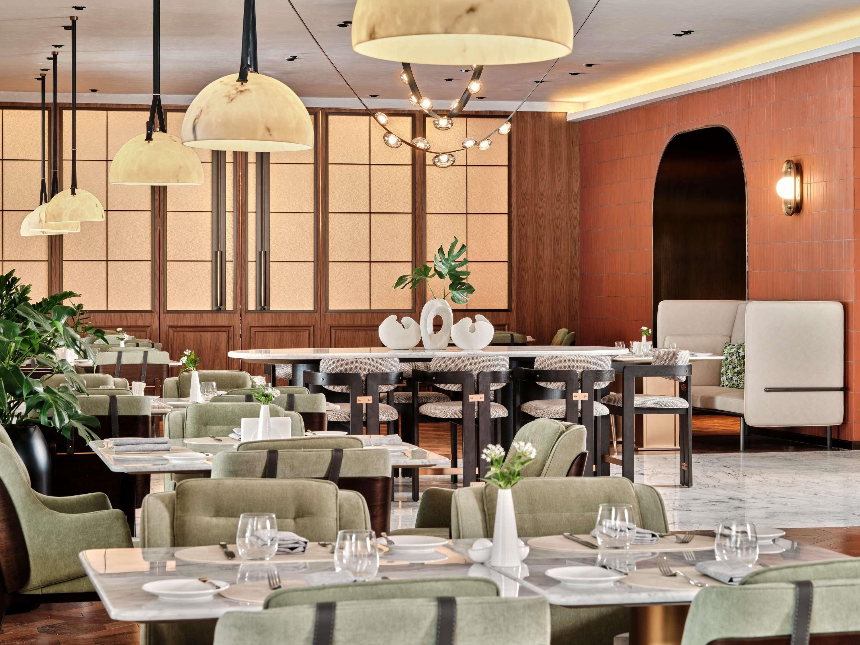 A restaurant with multiple tables and chairs, a chandelier, and a traditional Japanese-style wall.