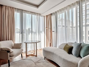 A modern living room with a sofa, a chair, a round table, and sheer curtains. - Swissôtel Tashkent (Tashkent)