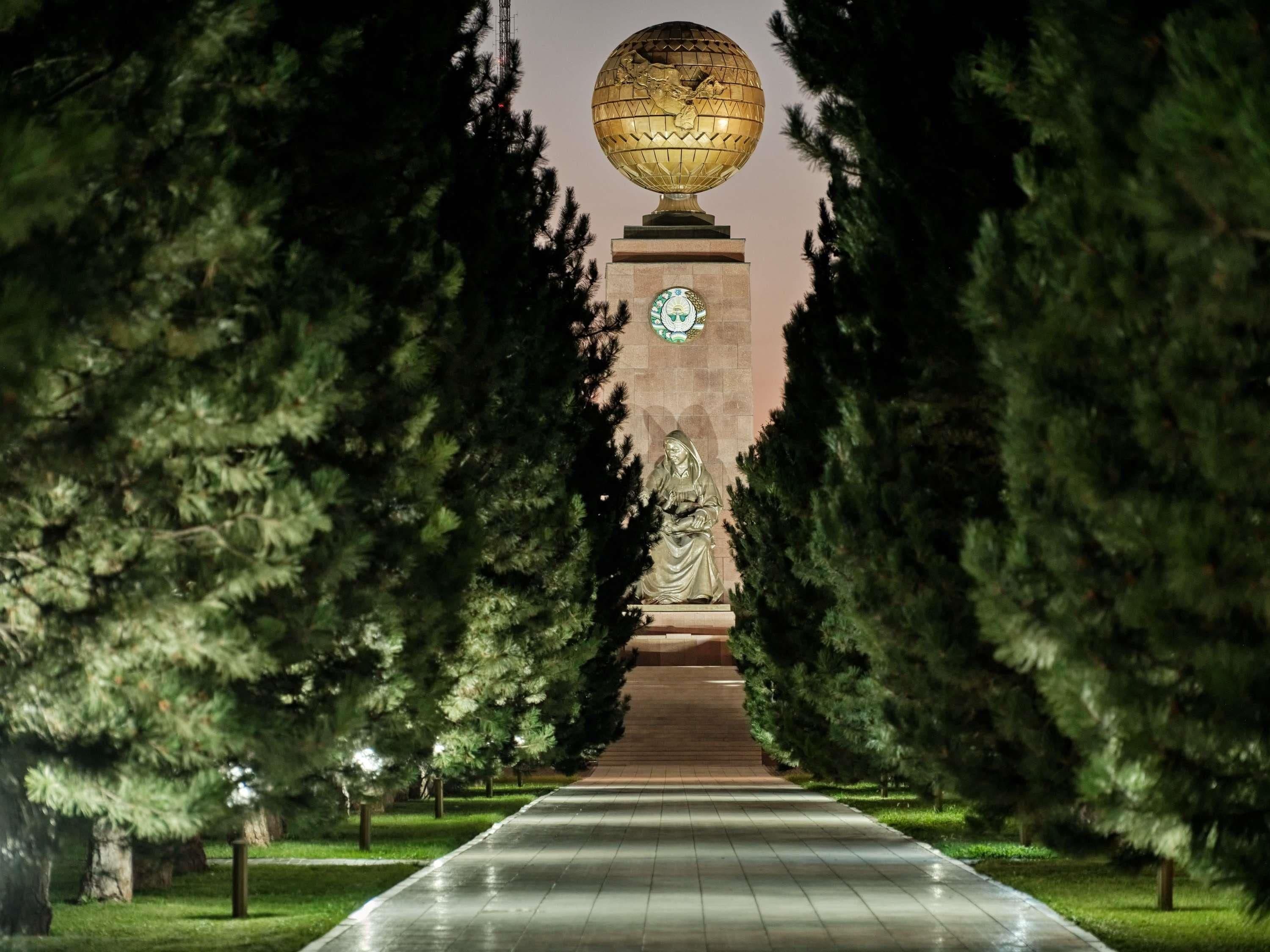 Un sendero bordeado por árboles que conduce a una estatua y un monumento esférico.