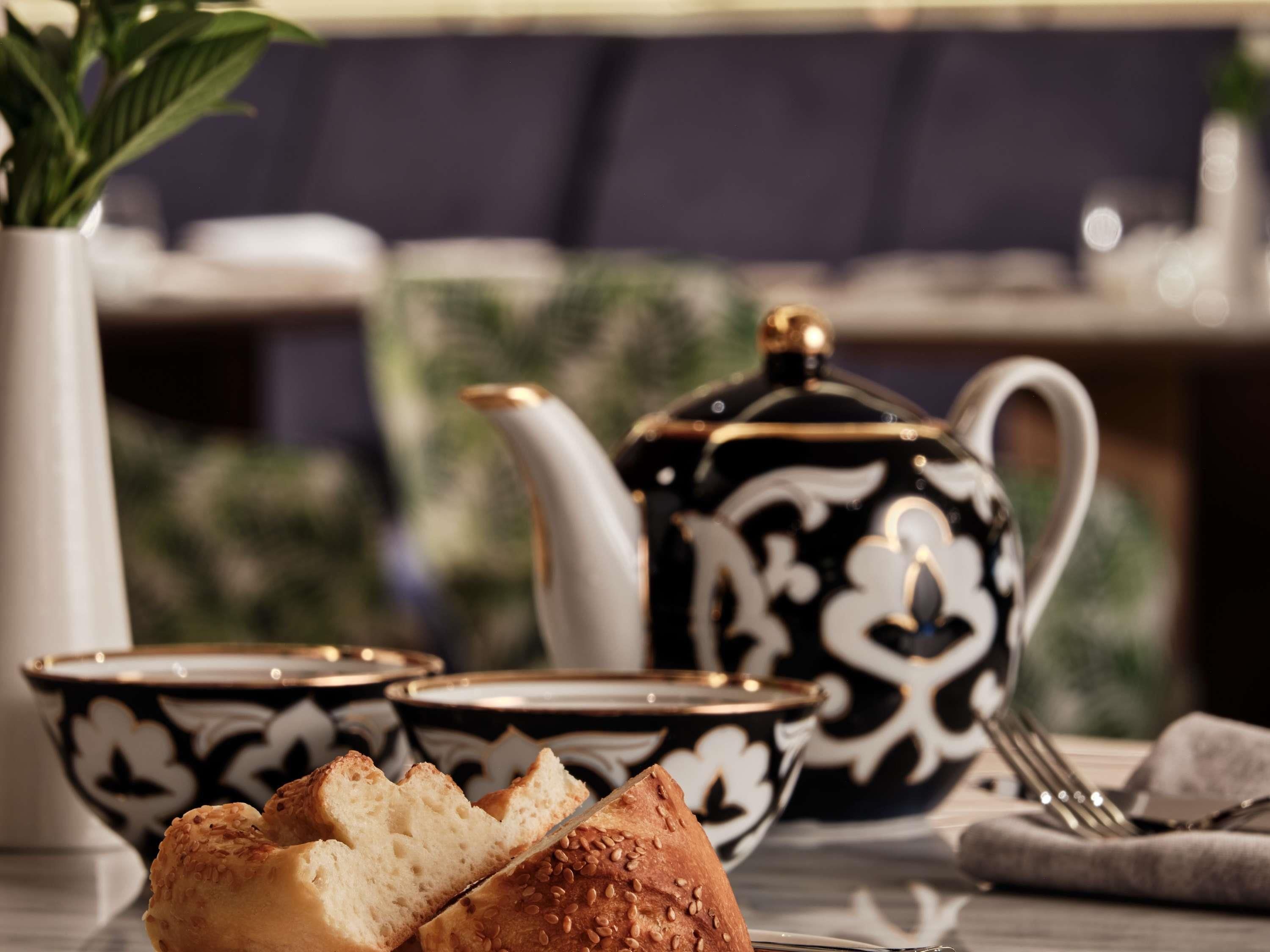 A table with a teapot, cups, and a slice of bread.