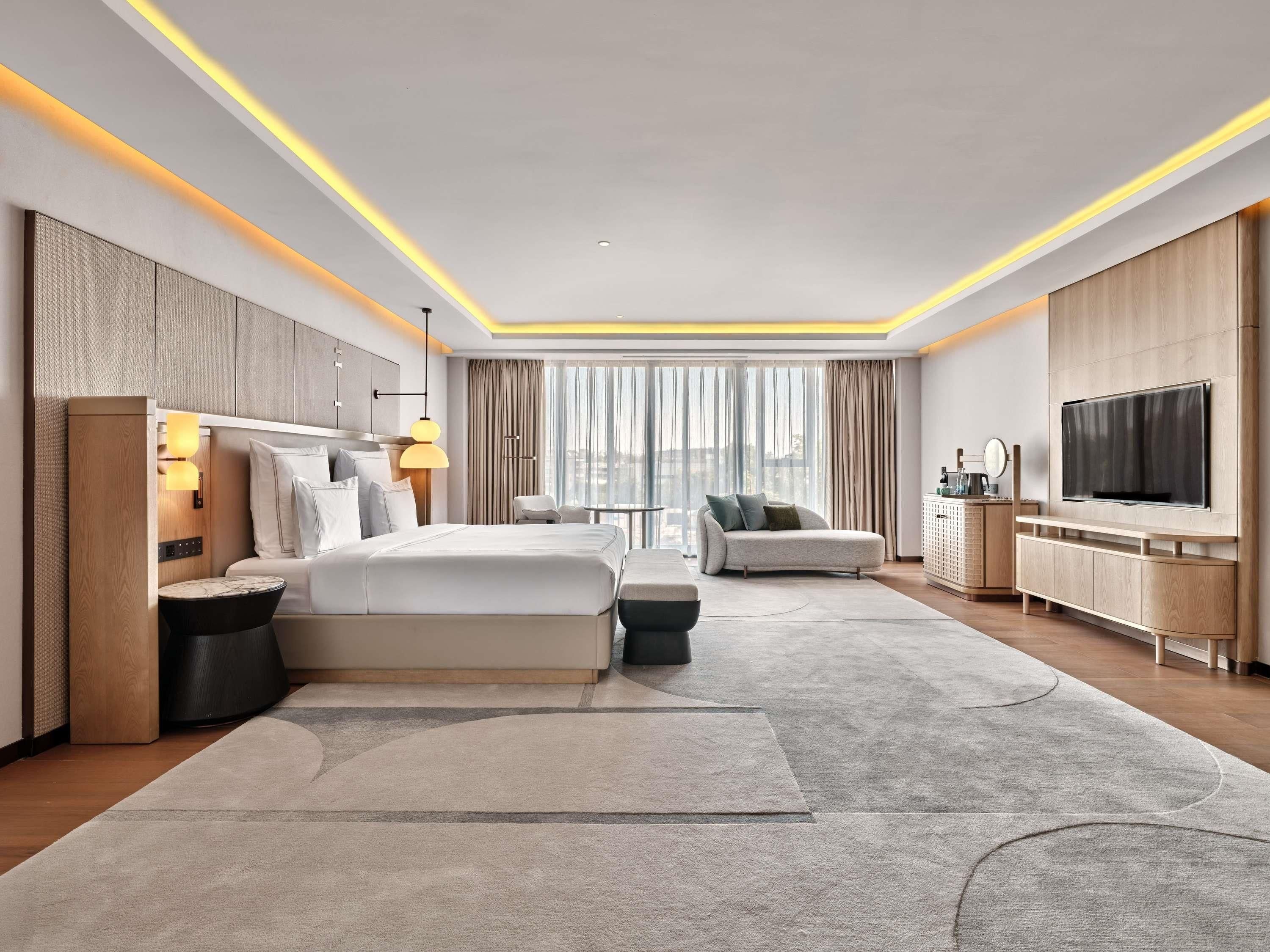 A modern hotel room with a large bed, a sofa, a TV, and a desk.