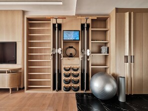 A modern room with a wooden wardrobe, a television, exercise equipment, and a black marble floor. - Swissôtel Tashkent (Tashkent)
