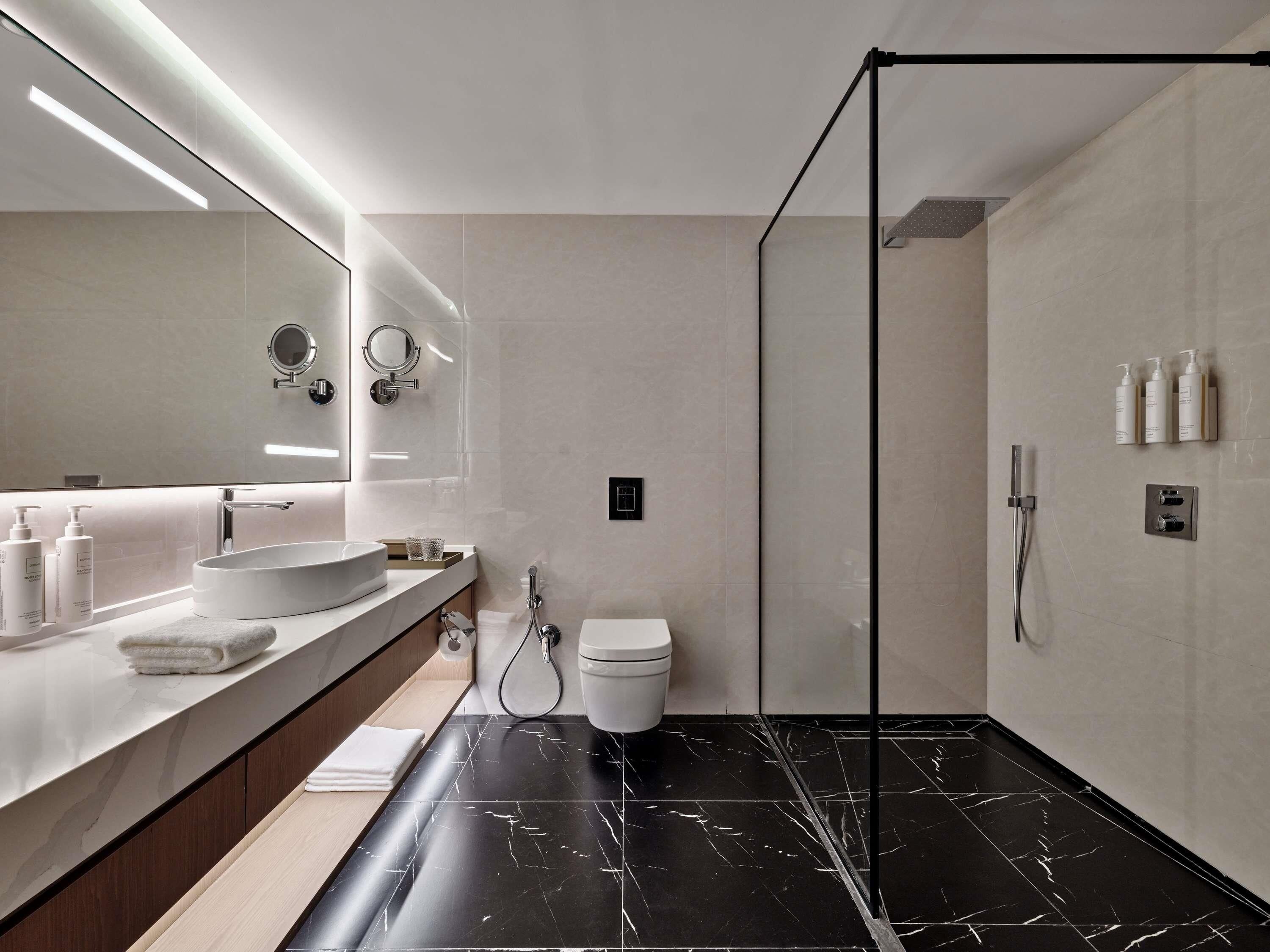 Un baño moderno con un espejo grande, un lavabo redondo, un inodoro y una zona de ducha.