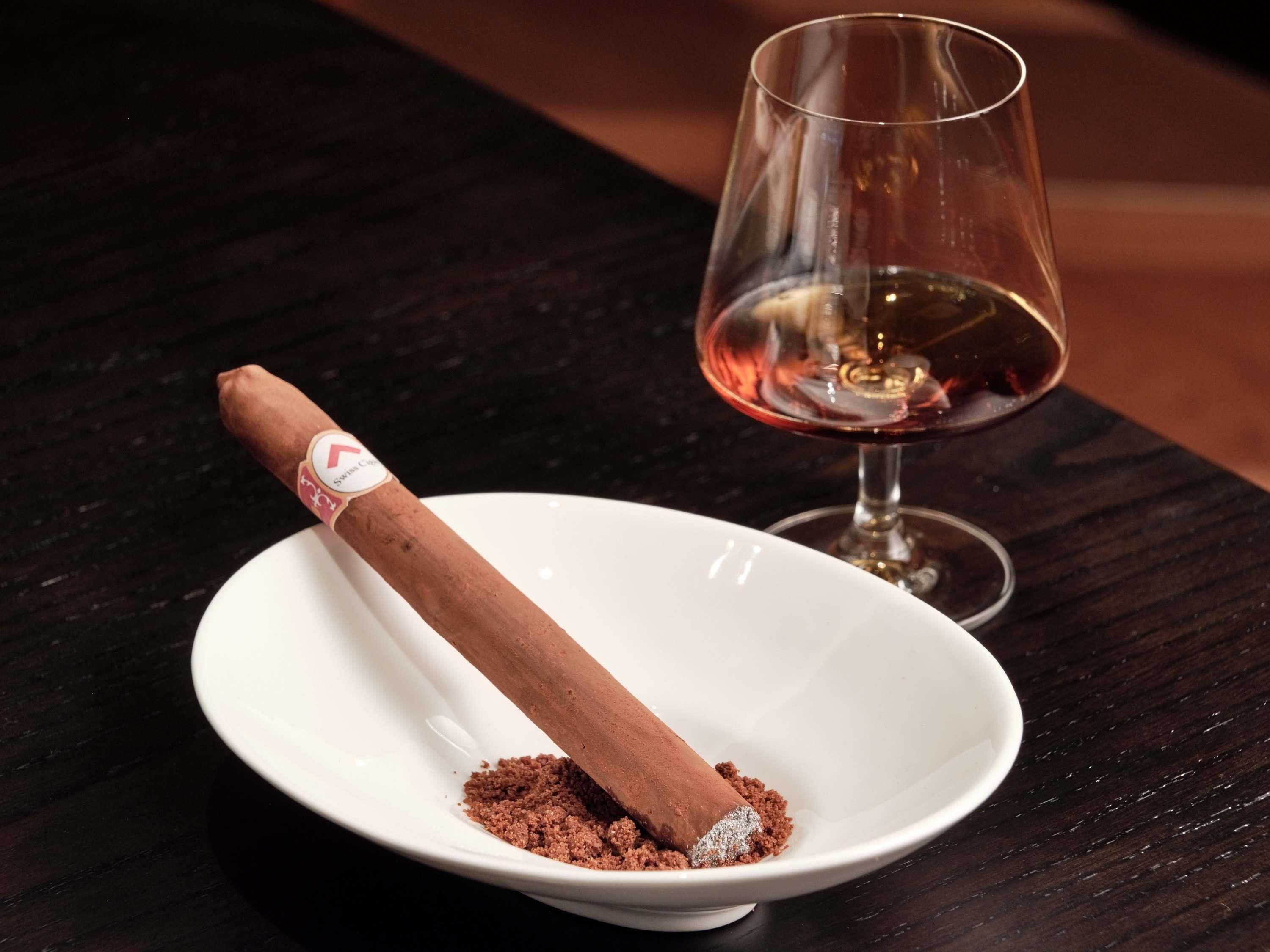 A cigar in a white bowl with a glass of red wine beside it.