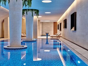 A modern indoor swimming pool with clear blue tiles, large columns, and lounge chairs along the walls. - Swissôtel Tashkent (Tashkent)