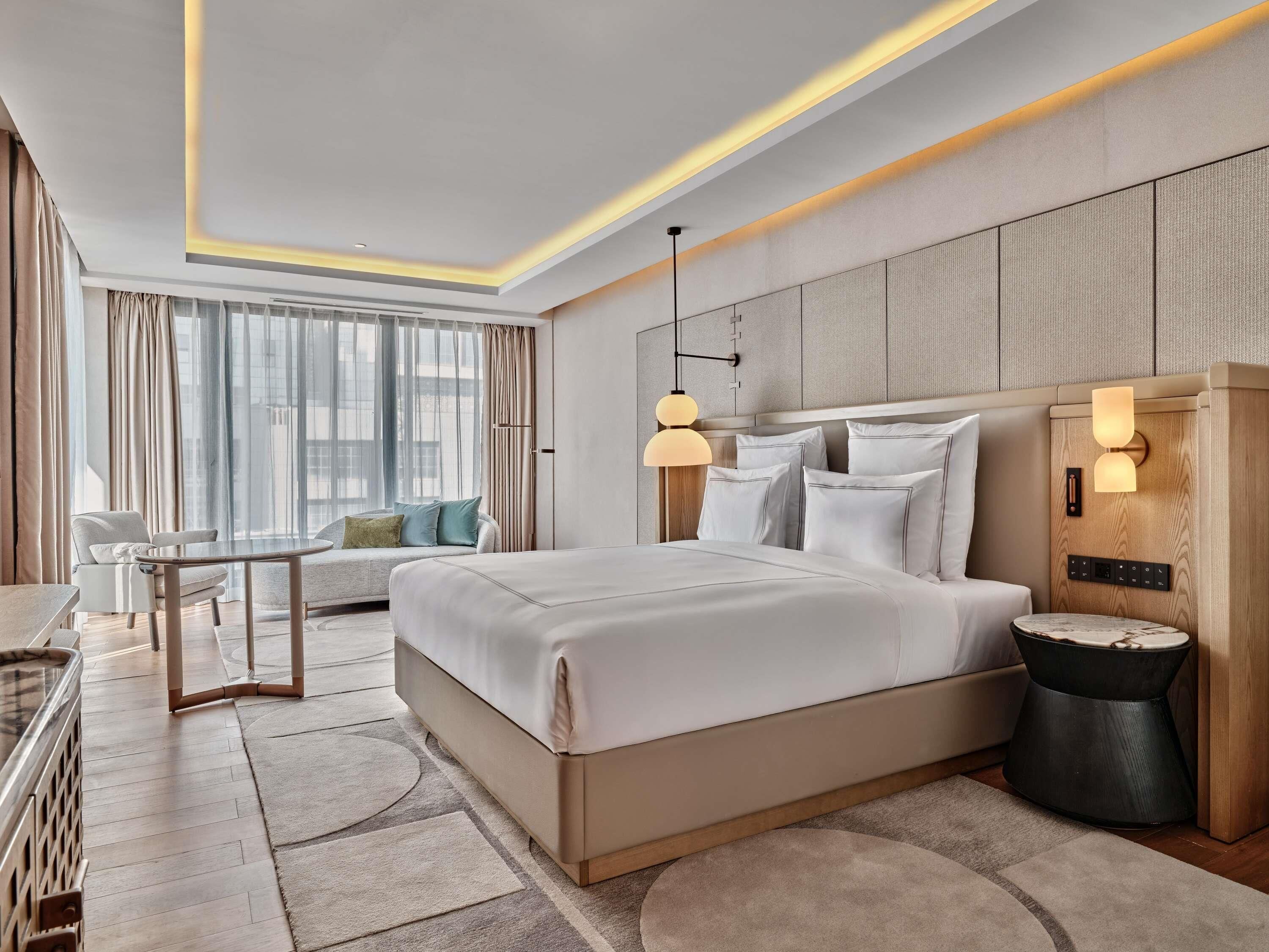 A modern hotel room with a large bed, a desk, and a sofa.