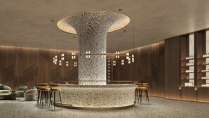 En modern entréhall med en central pelare, en bardisk, sittplatser och en utställning av olika föremål.