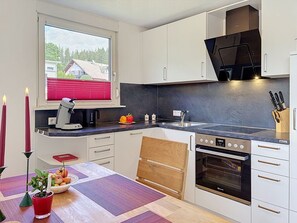 Een moderne keuken met witte kasten, een zwarte kookplaat en een raam met rode lamellen.