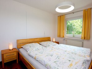 A bedroom with a wooden bed, two bedside tables, a night lamp, a window with curtains, and a radiator.