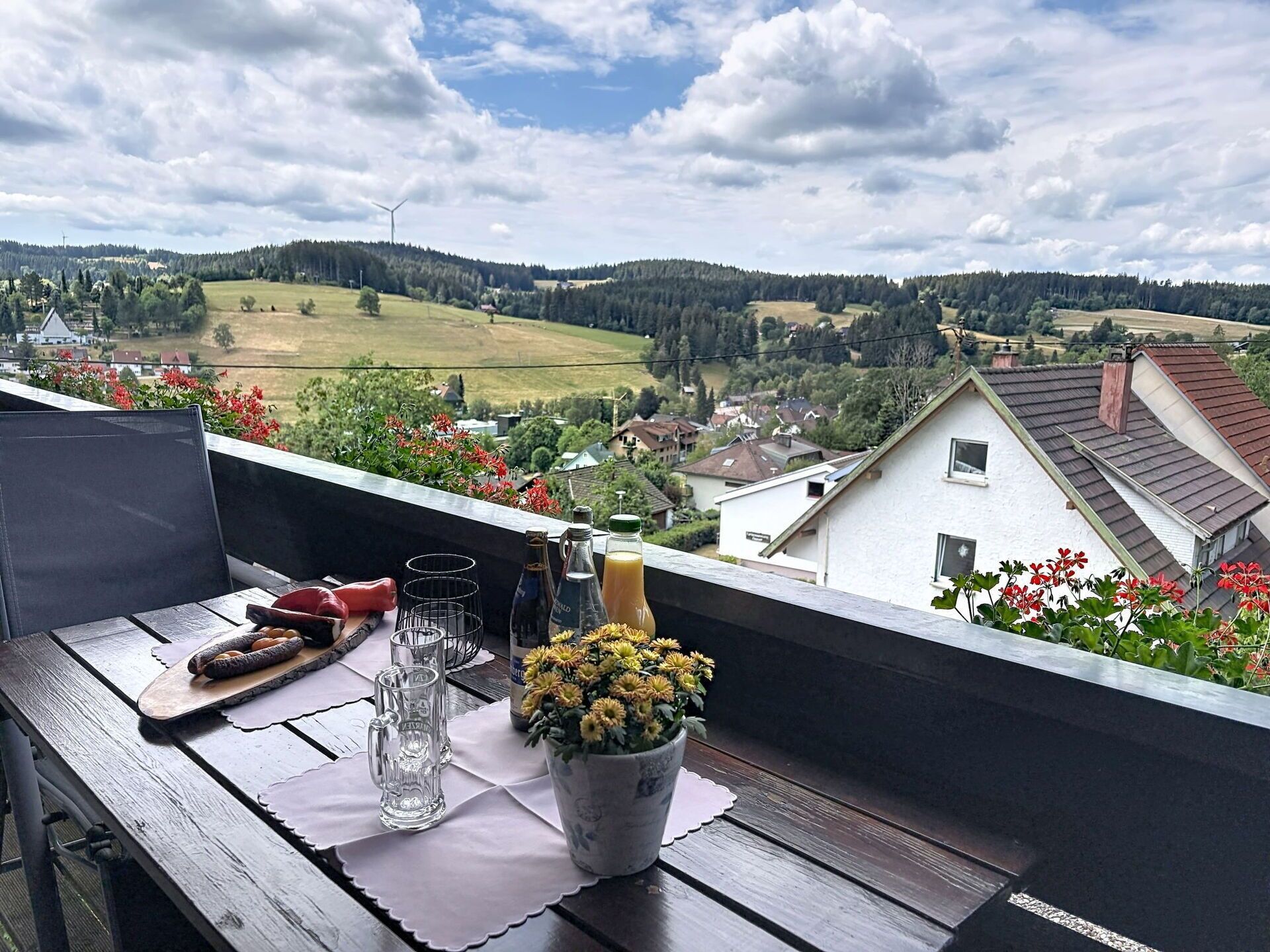 Een balkon met een eettafel, met uitzicht op een landelijk gebied met huizen en een windmolen.