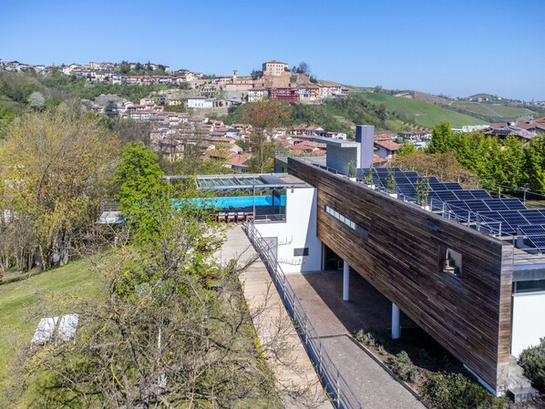 A modern building with a wooden facade and solar panels on the roof, overlooking a town with historic buildings and a hill in the background.