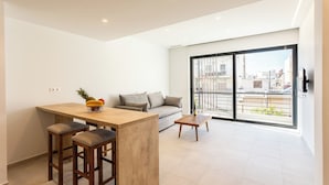 A modern living space with a kitchen area, a sofa, and a balcony with a city view. - Grec Suites Dafni, Athens Supreme Apartment by GrecCollection (Dafni)