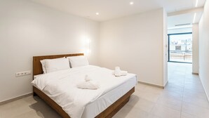 A modern hotel room with a wooden bed, white linens, and a view of the city through large windows. - Grec Suites Dafni, Athens Supreme Apartment by GrecCollection (Dafni)