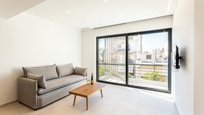 A modern living room with a grey sofa, a wooden coffee table, and a large sliding glass door leading to a balcony. - Grec Suites Dafni, Athens Supreme Apartment by GrecCollection (Dafni)