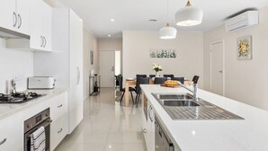 Une cuisine moderne avec des meubles blancs, un îlot central doté d’un évier et un coin repas à l’arrière-plan.