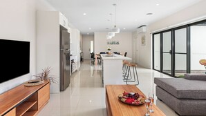 Une cuisine moderne dotée d’un îlot central, un coin repas avec une table dressée pour deux personnes et un salon avec un canapé et une table basse.