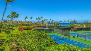 A tennis court with a view of the ocean and palm trees. - Regency Villas 212 Lush Garden By Suite Paradise (Koloa)