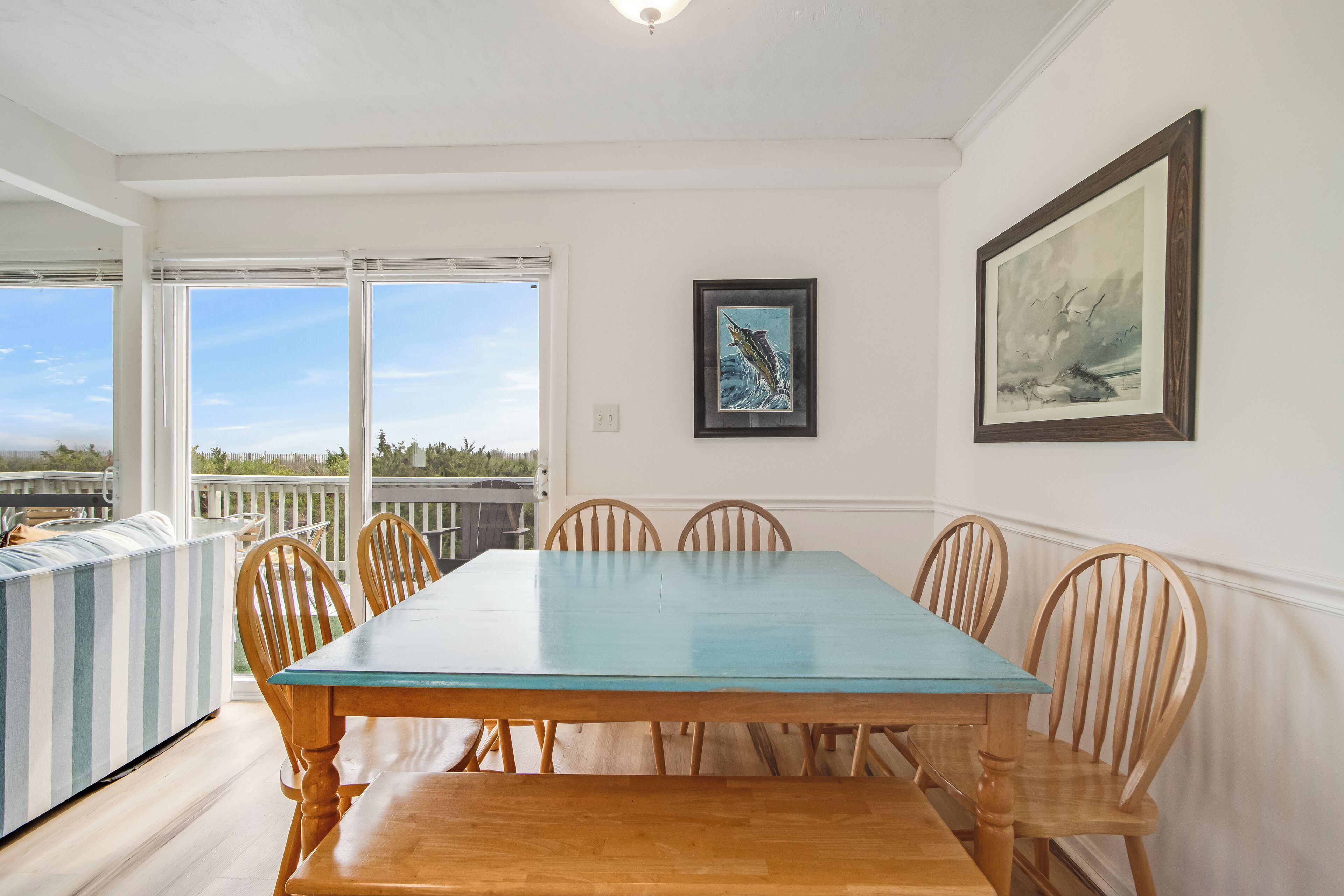 Une salle à manger avec une grande table et six chaises, un tableau encadré au mur et une vue à travers une porte vitrée.