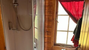 Une petite salle de bain rustique, avec des murs en bois, une douche vitrée, des toilettes et une fenêtre ornée d’un rideau rouge.