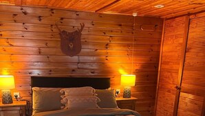 Une chambre aux murs lambrés, avec un lit, deux lampes de chevet et une tête d’animal fixée au mur.