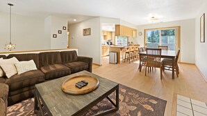 Un salon moderne avec un canapé d’angle marron, une table basse en bois et un coin repas comprenant une table et des chaises en bois.
