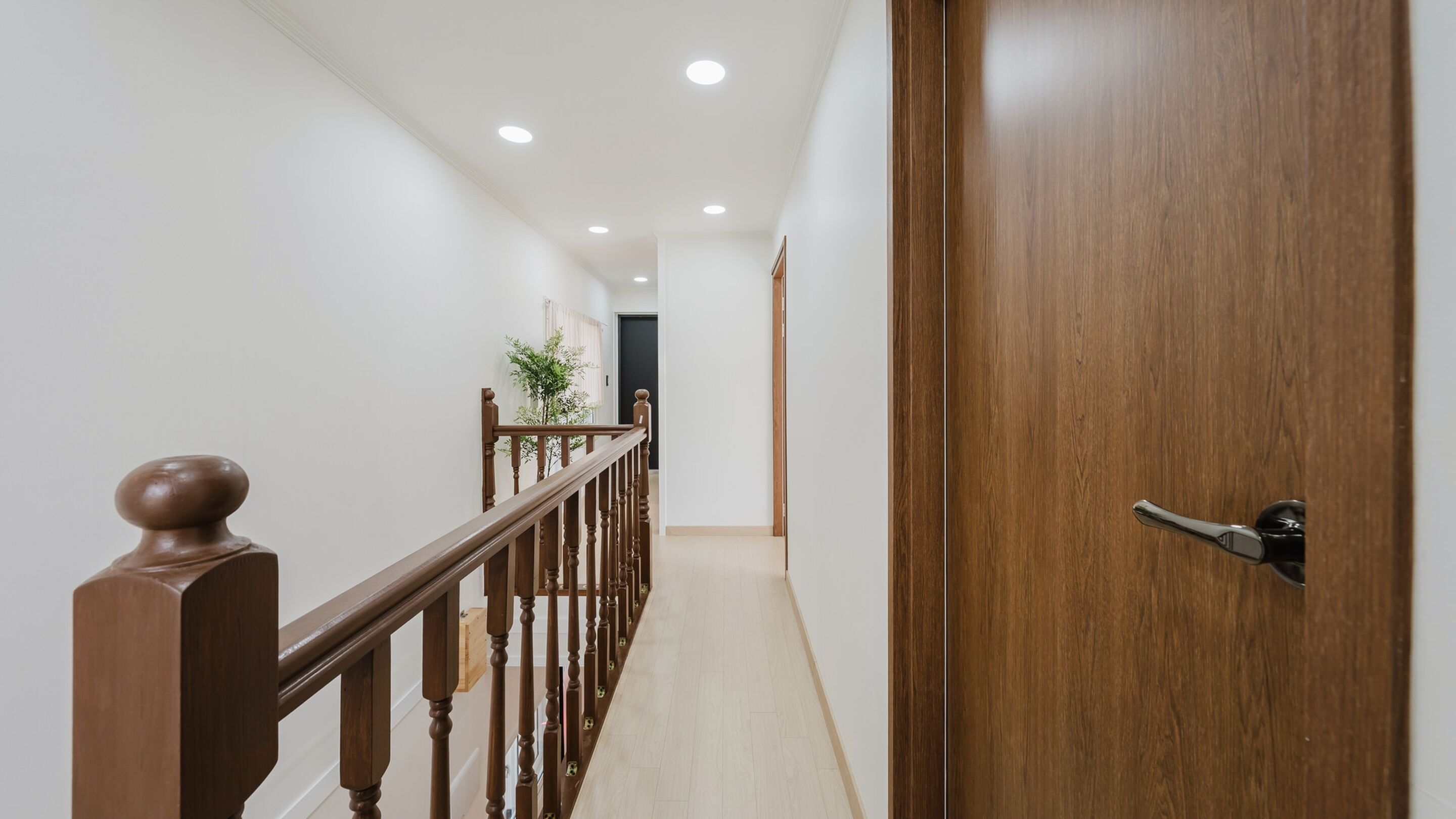 A hallway with a wooden railing, a wooden door, and a plant in the distance.