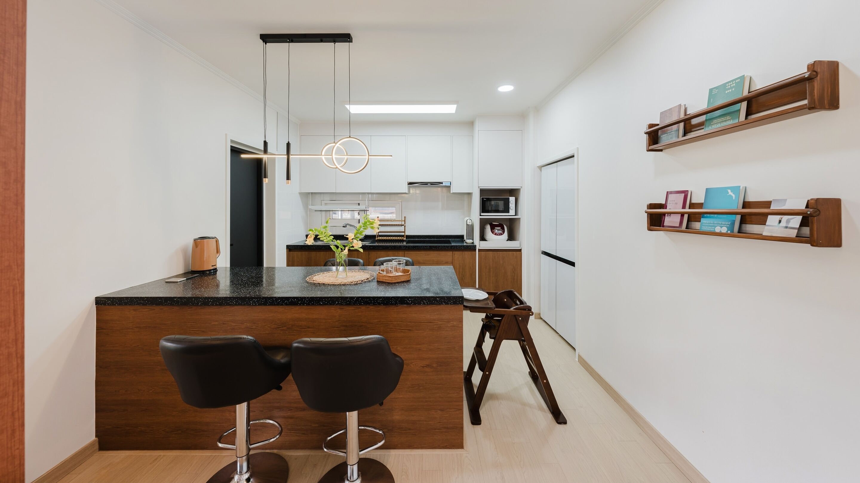 Una cocina moderna con una isla central, dos taburetes de bar, una lámpara colgante y estantes empotrados.