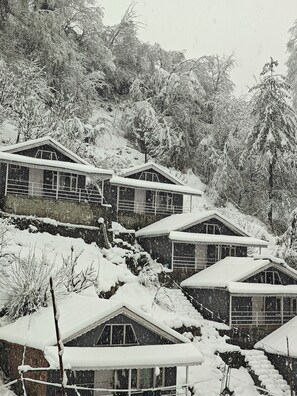A row of cabins on a snowy hillside, each with a pitched roof and windows. - New Rock Cottage (Manali)