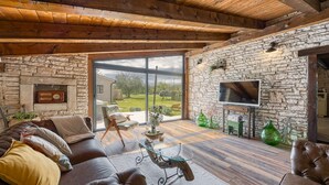 A cozy living room with a stone fireplace, leather sofa, and a large TV on a stone wall. - Villa Capadinka With Whirlpool (Marcana)