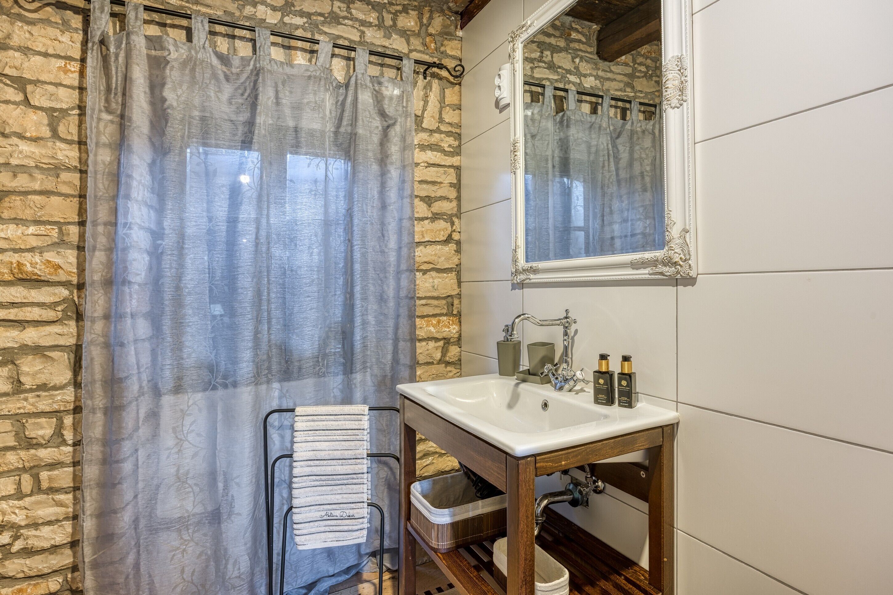 Une salle de bain avec un mur en pierre, un lavabo en bois, un miroir et un porte-serviettes.