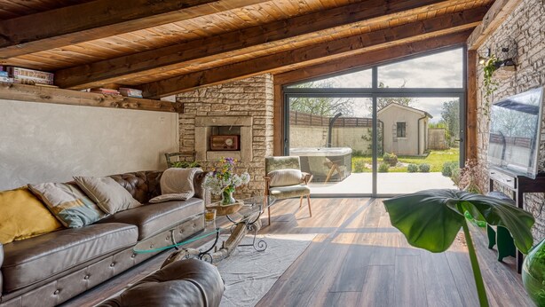 A cozy living room with a stone fireplace, leather sofa, and a large window offering a view of the outdoors. - Villa Capadinka With Whirlpool (Marcana)