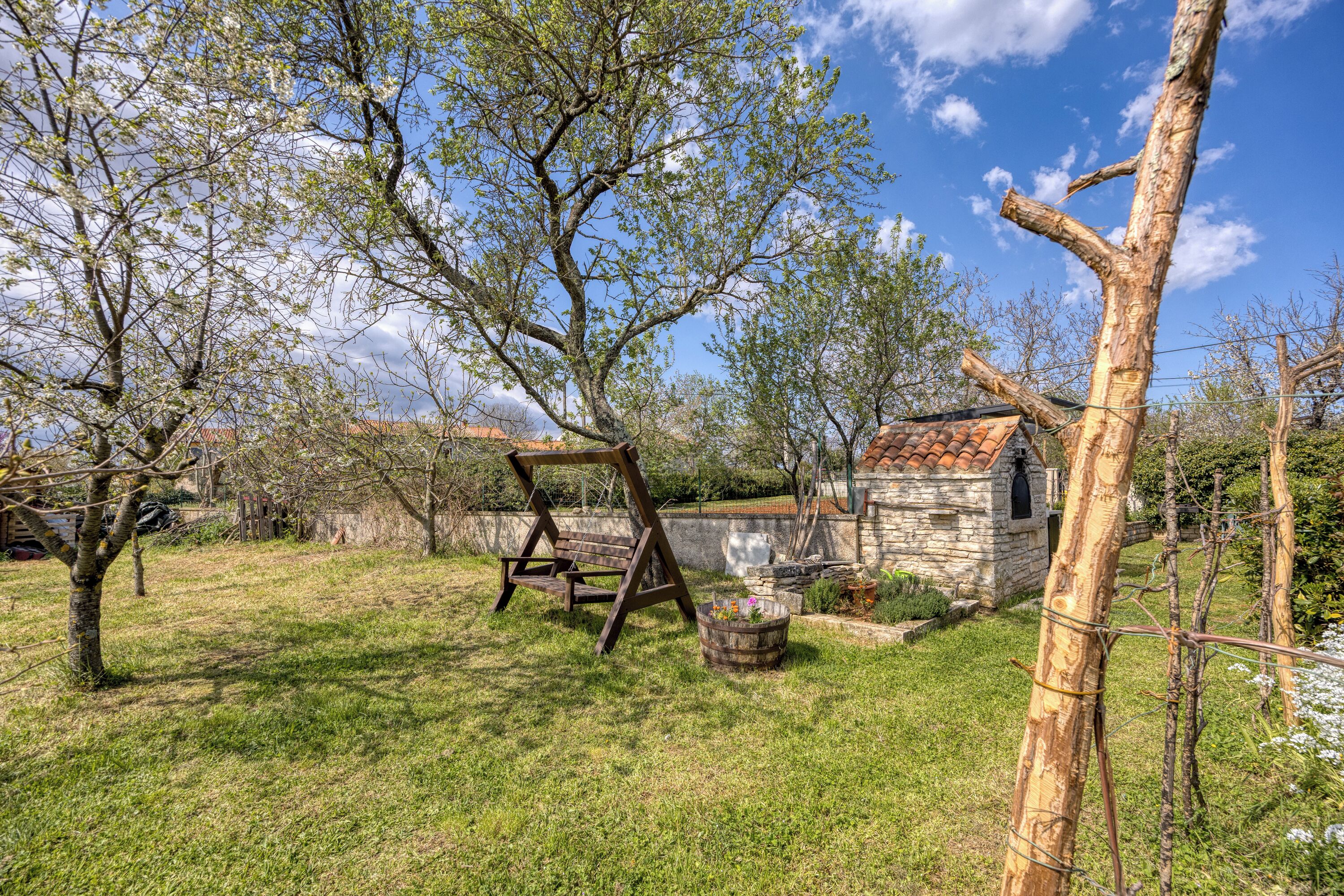 A rustic outdoor area with a swing set, a stone building, and a wooden fence.