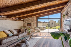 A spacious living area with a stone fireplace, leather sofa, and a large window offering a view of the outdoors. - Villa Capadinka With Whirlpool (Marcana)