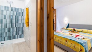 Un bagno con doccia, un portascopino e un letto con copripiumino colorato.