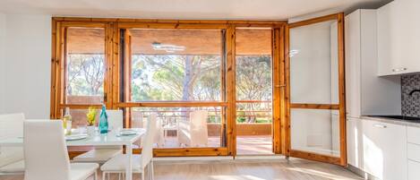 A modern kitchen with white cabinets, a dining area with white chairs, and large windows with a view of trees.