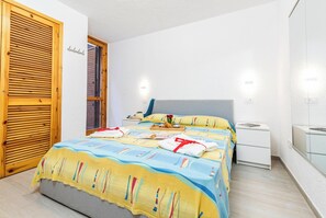 A bedroom with a bed, bedside table, and a wooden door. - Marcos Home (Olbia)