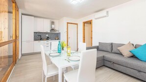 A modern kitchen with white cabinets, a black and white backsplash, and a dining area with a glass table and white chairs. - Marcos Home (Olbia)