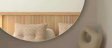 Una habitación moderna con un espejo redondo, un cabecero de madera y una escultura minimalista sobre una repisa de madera.