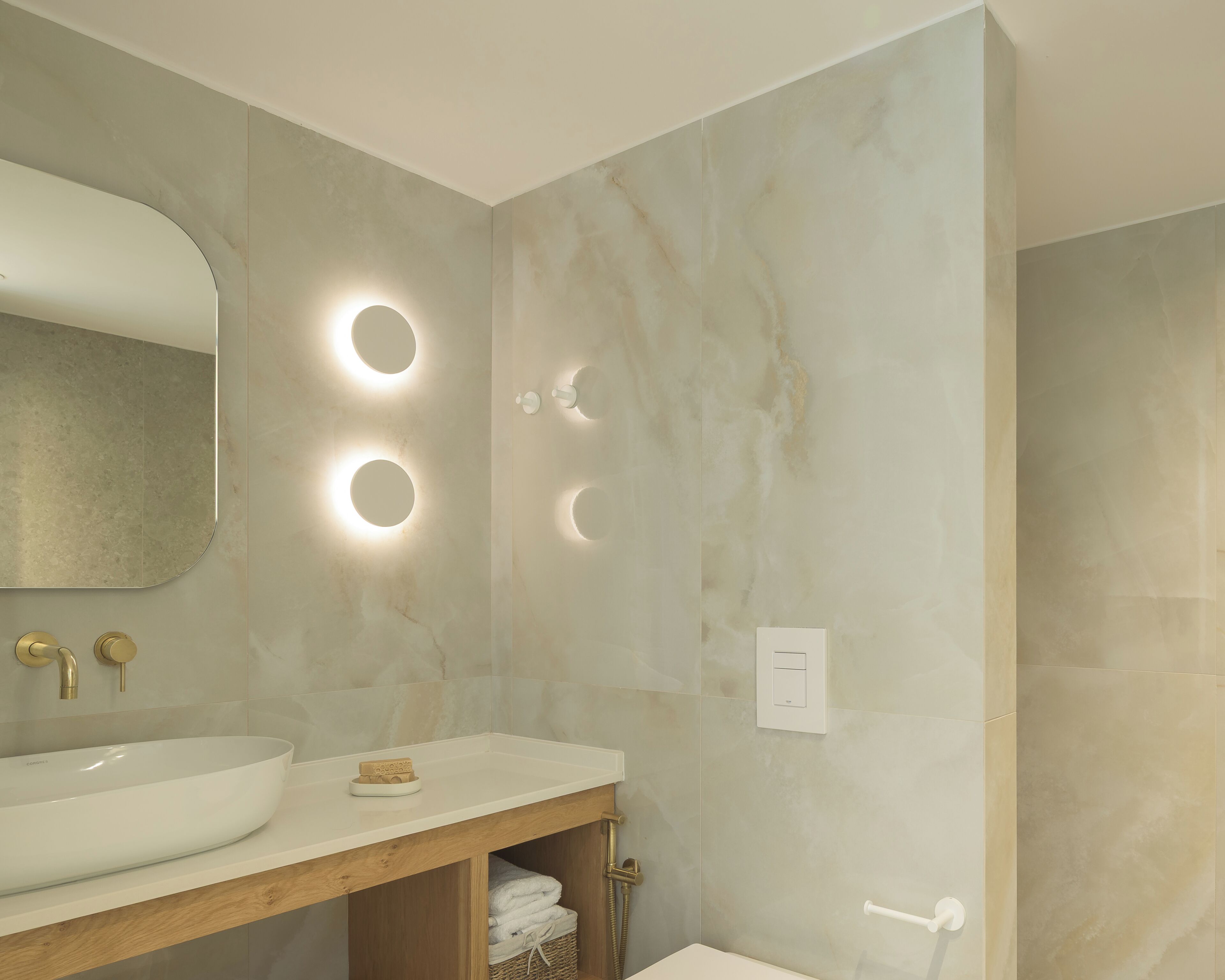 A modern bathroom with a large oval sink, a wooden vanity, a mirror, and three wall-mounted lights.