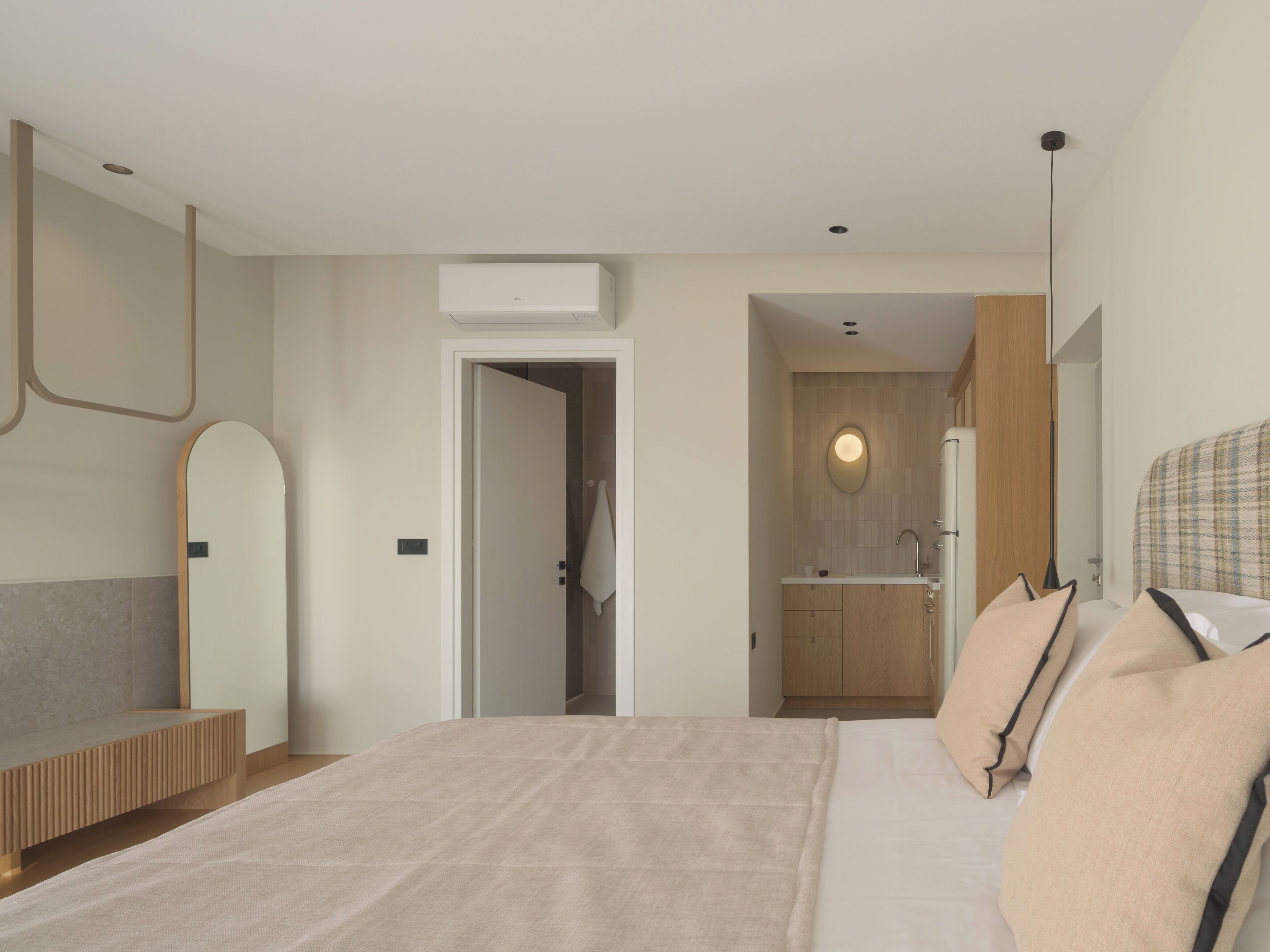 Ein modernes Schlafzimmer mit einem großen Bett, einer hölzernen Bank, einem Spiegel und einem durchgegangene Tür erkennbaren Badezimmer.