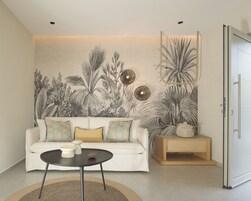 Una sala de estar con un sofá blanco, una mesa de centro redonda y un tapiz de plantas tropicales en la pared.