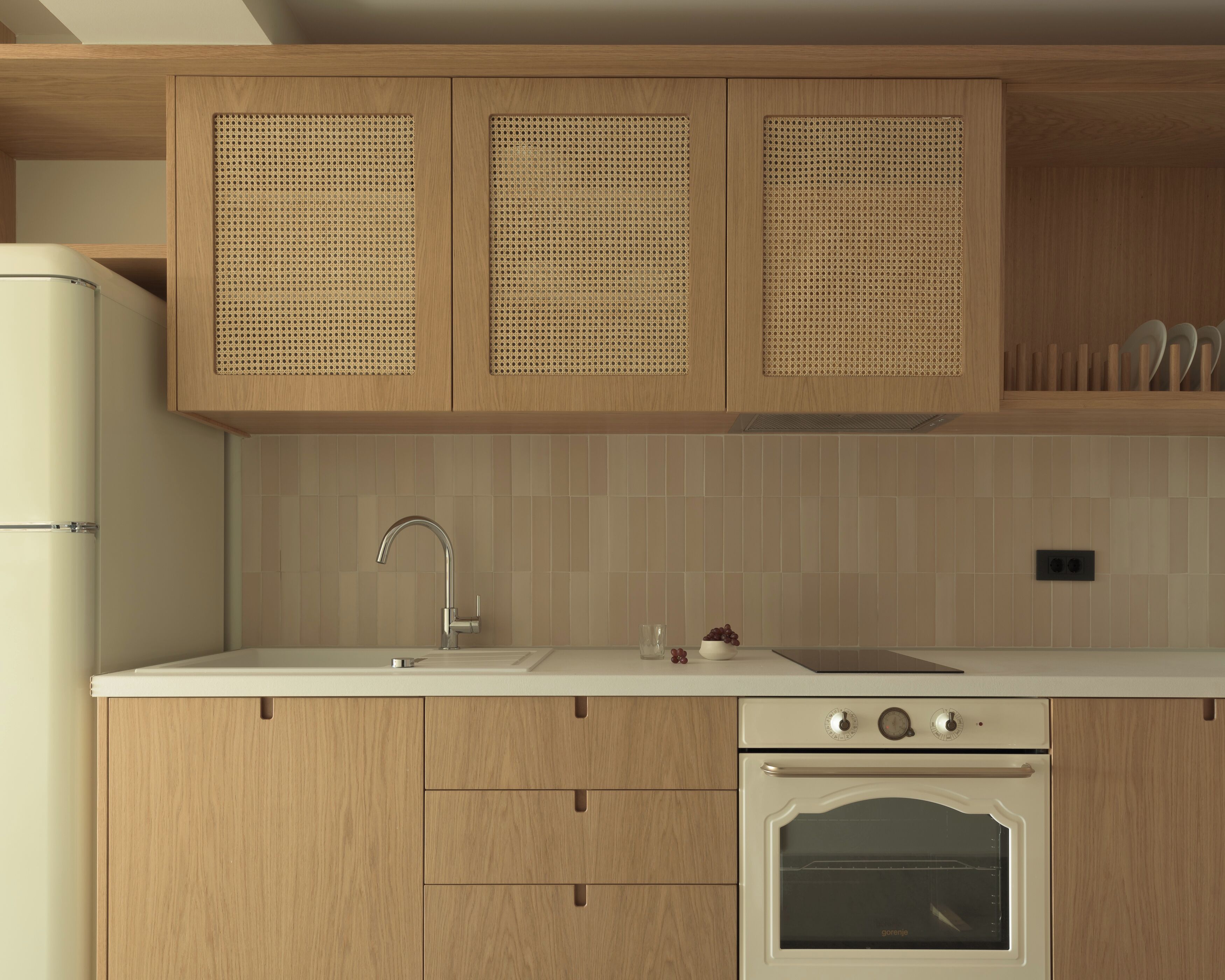 Una cocina con armarios de madera, encimera blanca, fregadero y horno empotrado.