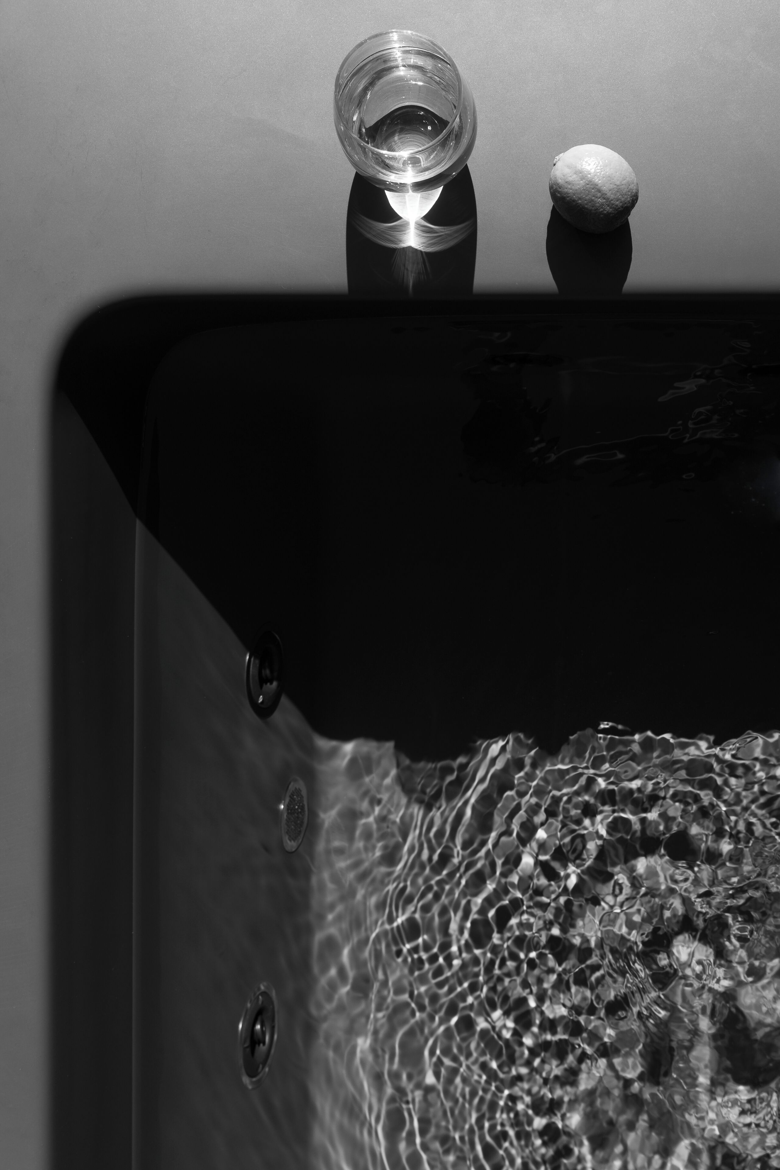 A black and white photo of a bathroom sink with a clear glass, a stone, and water.