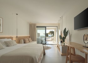 Habitación de hotel moderna con una cama grande, un escritorio, un televisor y un balcón con vistas al mar.