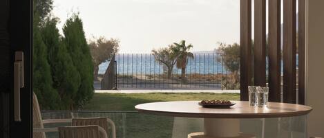 A modern balcony with a round table and chairs, overlooking a coastal landscape with a fence and trees.