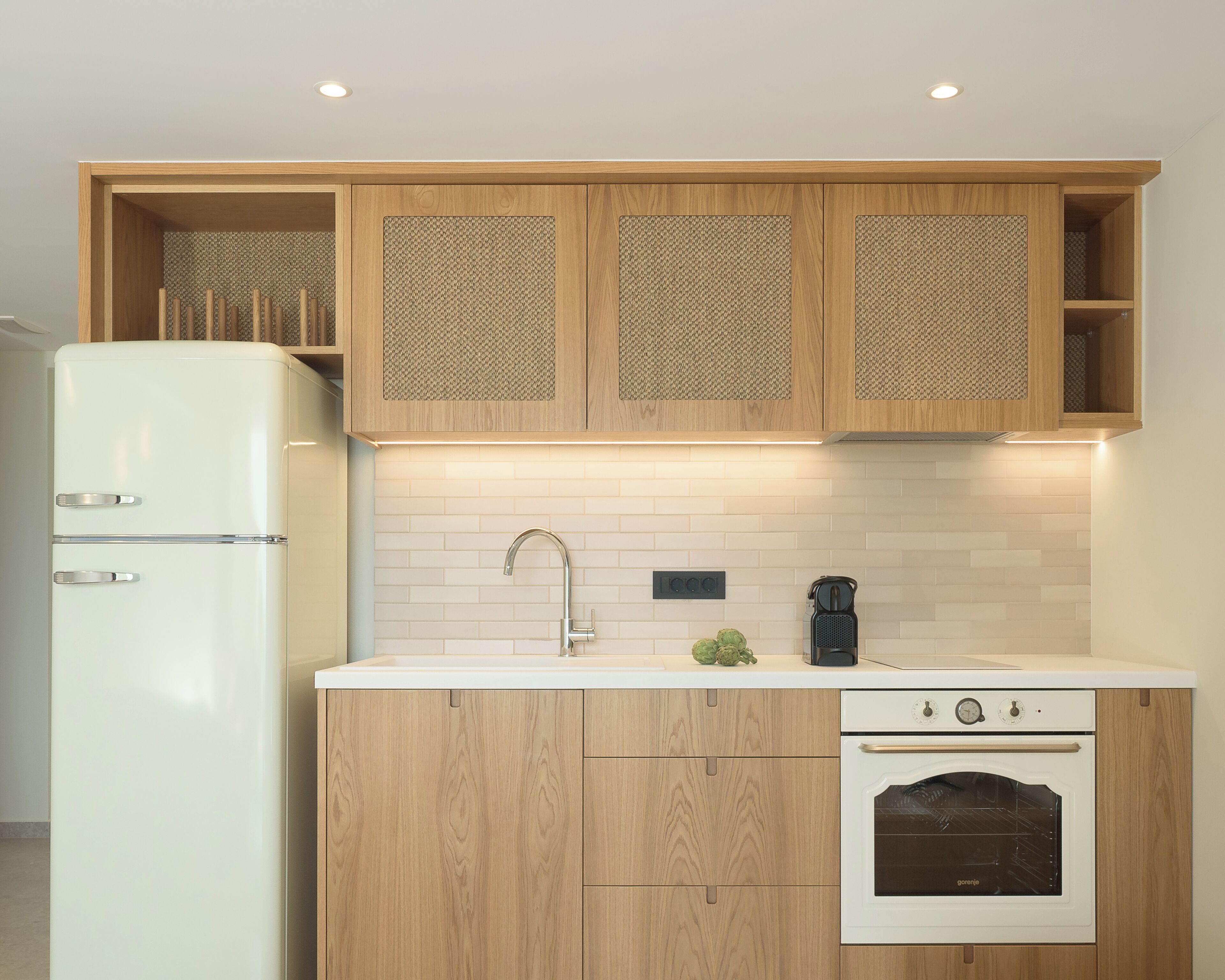 A compact kitchen with wooden cabinets, a white refrigerator, a sink, and a built-in oven.