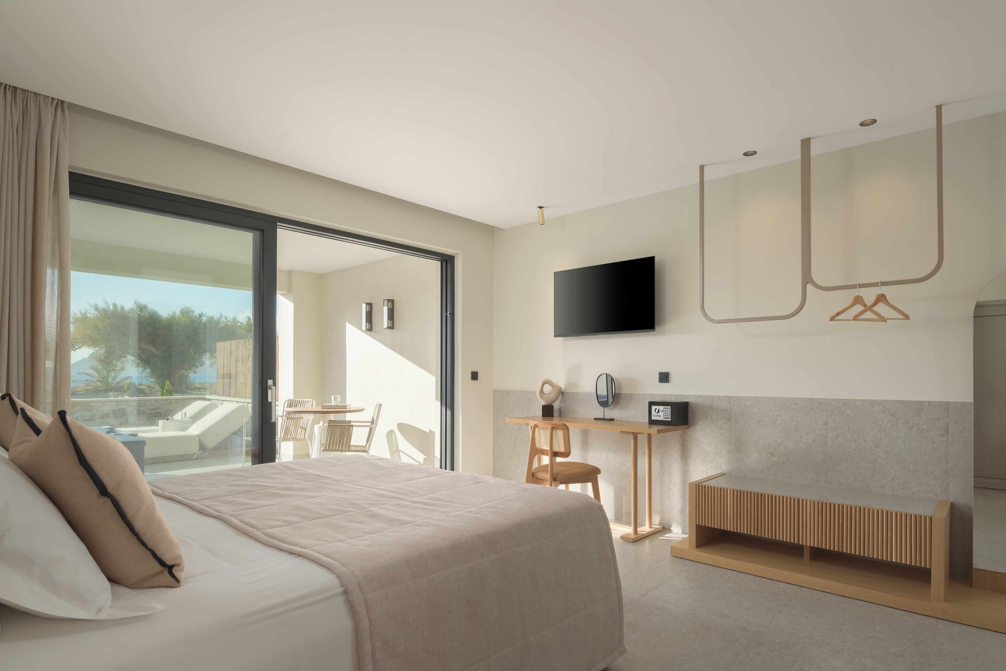 A modern hotel room with a large bed, a desk, a TV, and a balcony with a view of the outdoors.