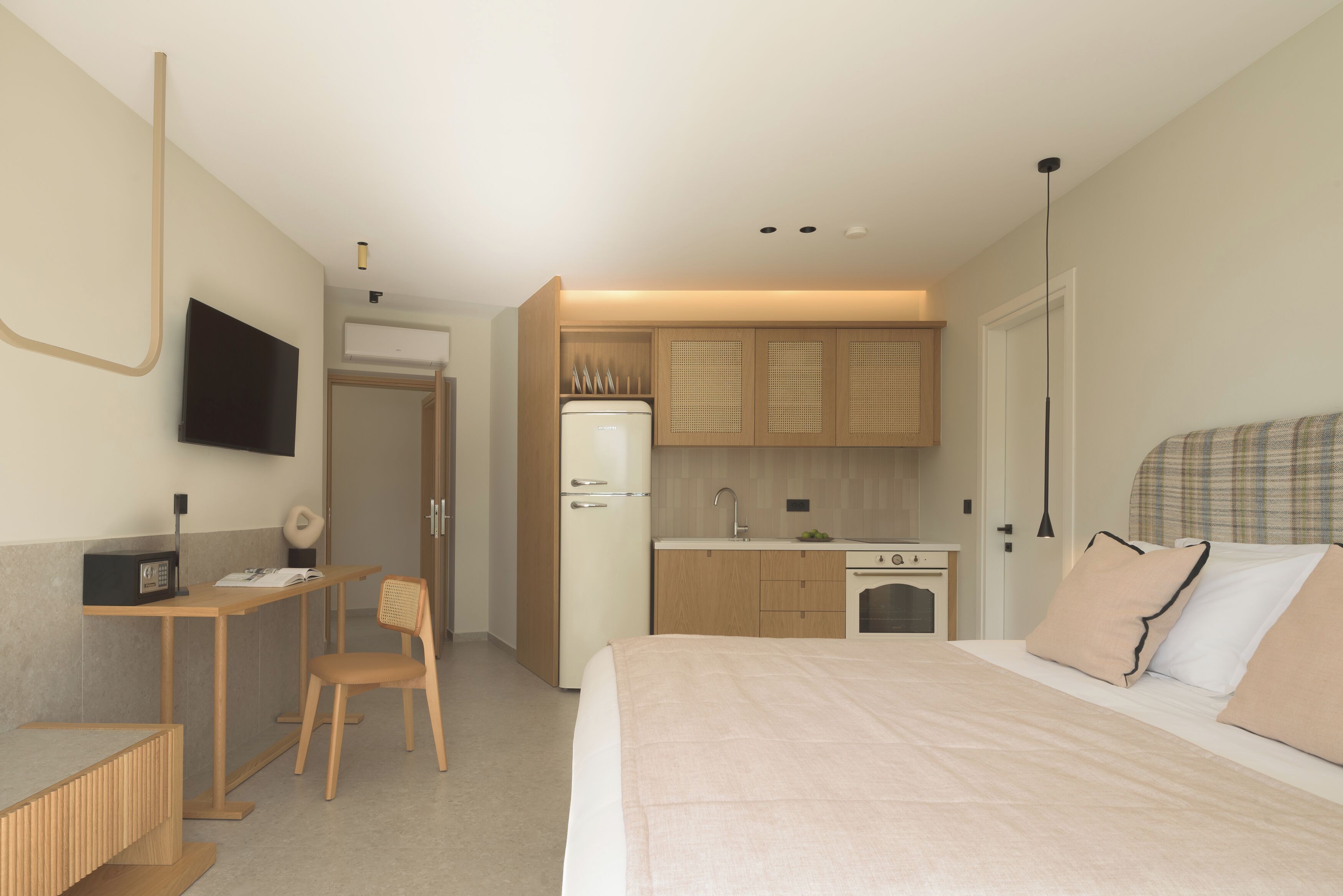 Una habitació d'hotel moderna amb llit, escriptori, cadira, televisió, cuina americana i bany.