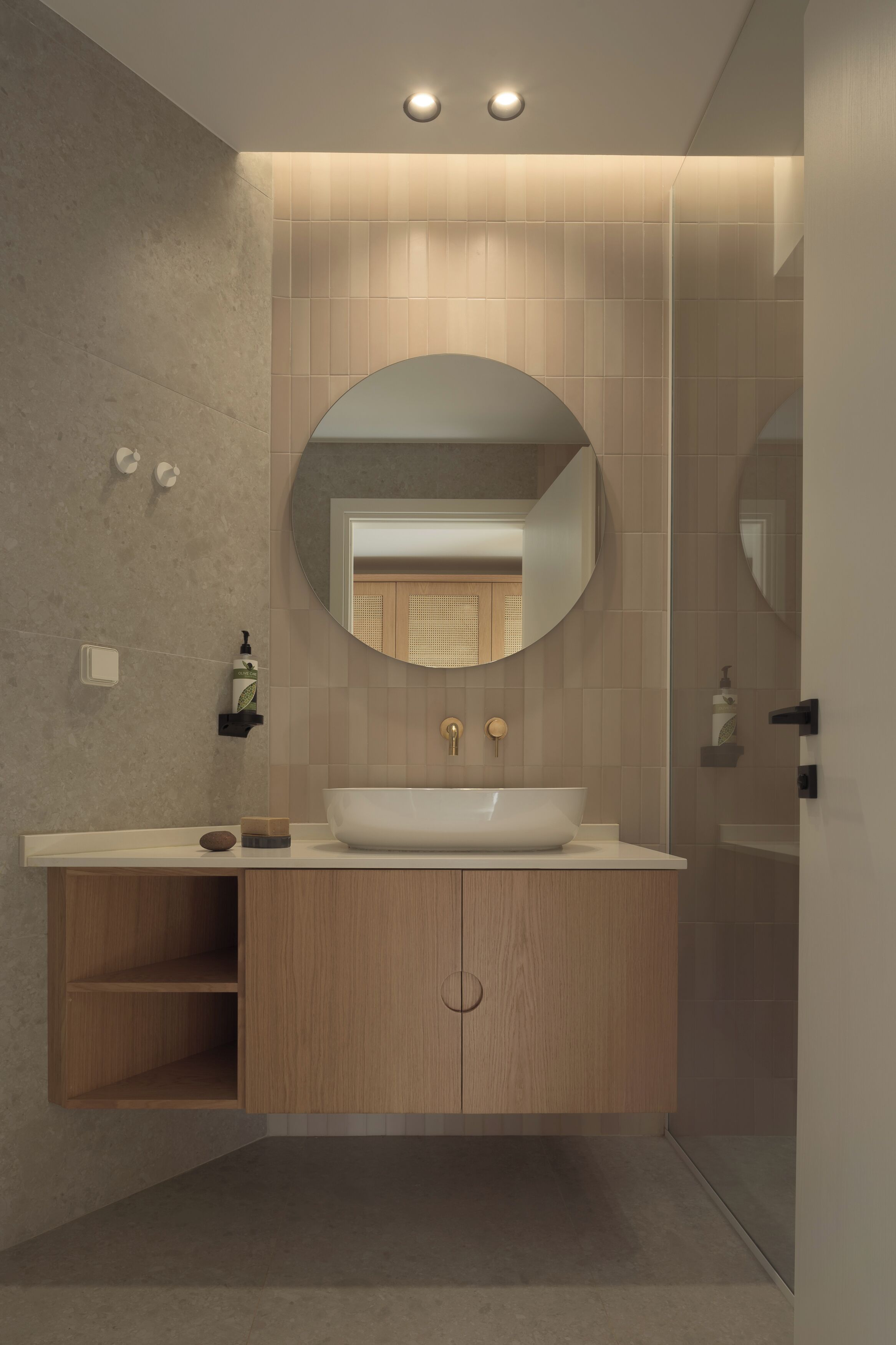 Un bagno moderno con uno specchio rotondo, un lavandino bianco, mobili in legno e un angolo doccia.